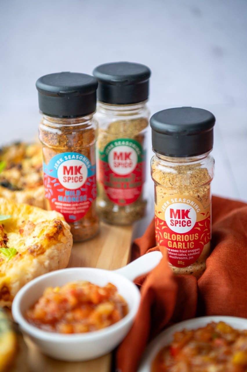 MK Spice Mild Madness and Glorious Garlic jerk seasonings on a table with food and salsa