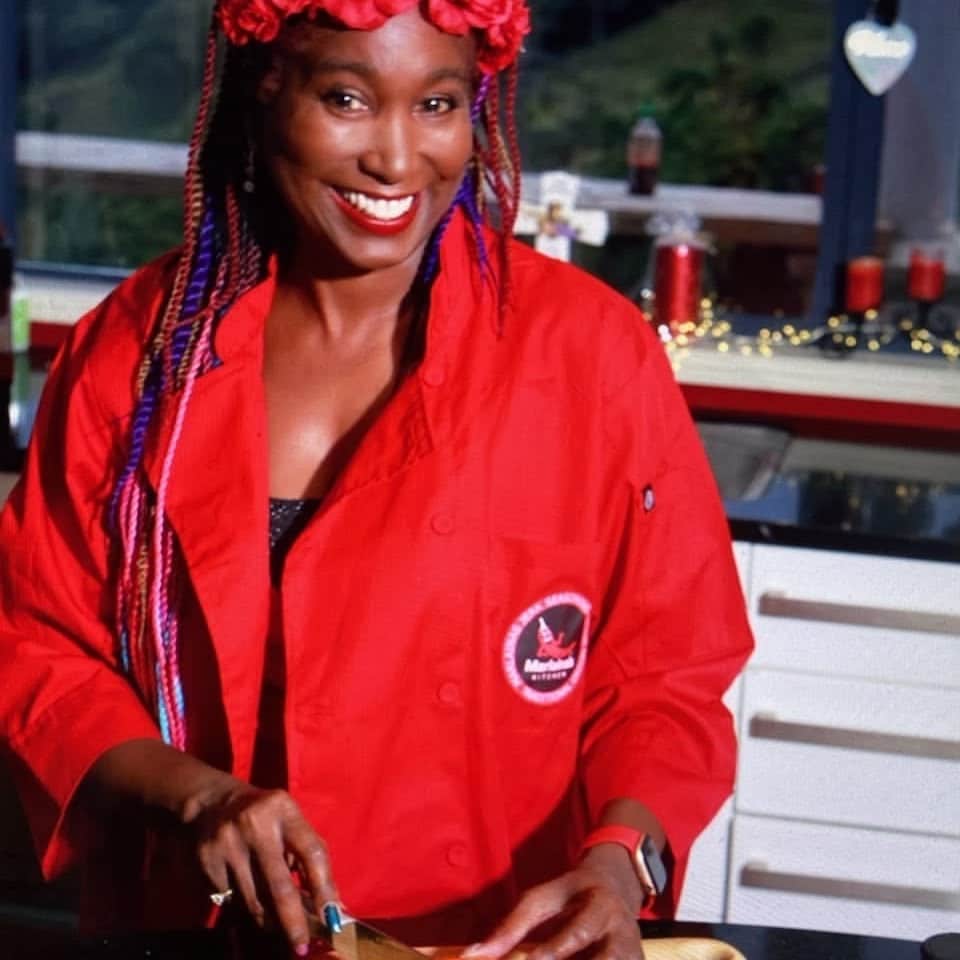 Marlaina Curtis, founder of MK Spice, smiling in a red chef's jacket while slicing a capsicum in her kitchen
