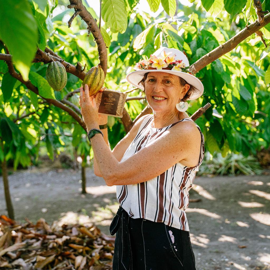 Bronwyn O'Hara of MALVA Chocolate holding a Bean to Bar chocolate bar beside a cacao pod on the tree