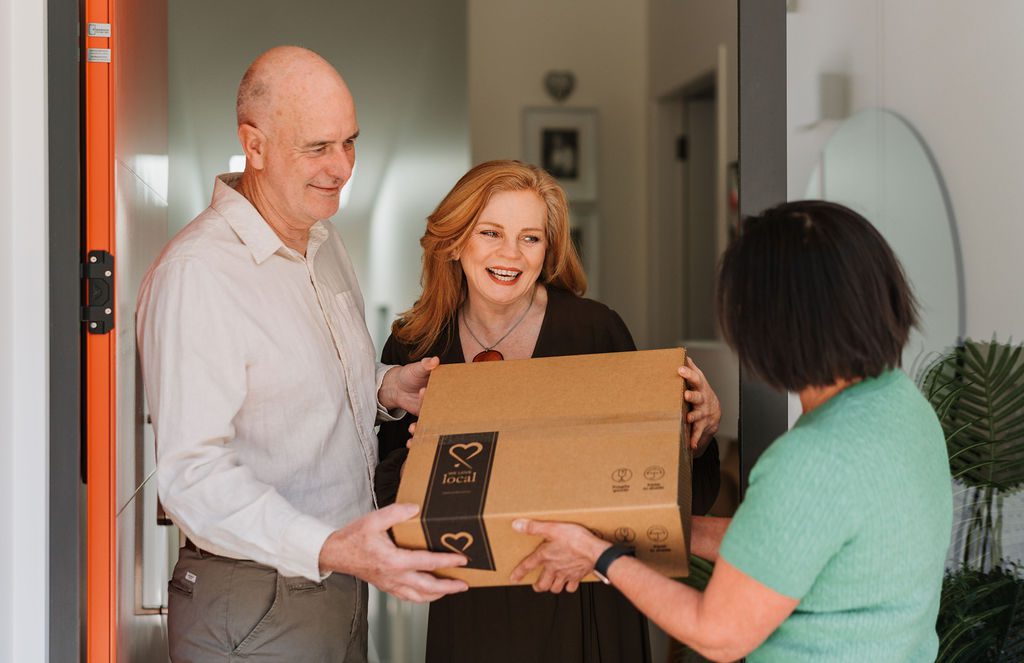 An older couple receiving a We Love Local gift box at their front door